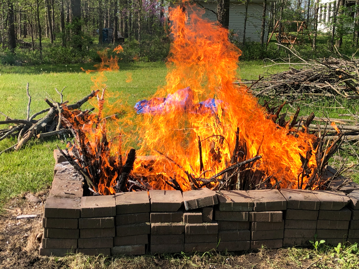 A raging fire in a barbecue pit with a green field behind it.