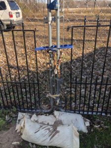 A heavily chained chain link gate with sandbags at ground level.