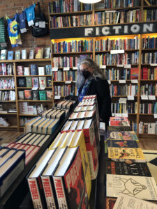 A woman in black with gray hair and a floral blue scarf browses books.