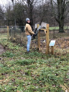 Tall woman smiling at camera as she wraps hoses on a fence post in a yard.