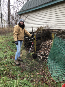 Tall woman outdoors with shovel near compost pile.