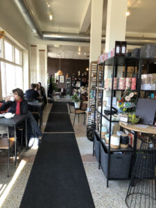 A long black carpet separates a row of tables from a shopping area. 