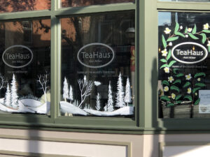 Storefront with winter scene of pine trees painted white on windows. The name "TeaHaus" appears above the winter scene.