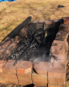 smoldering black logs inside brick fireplace in a field.