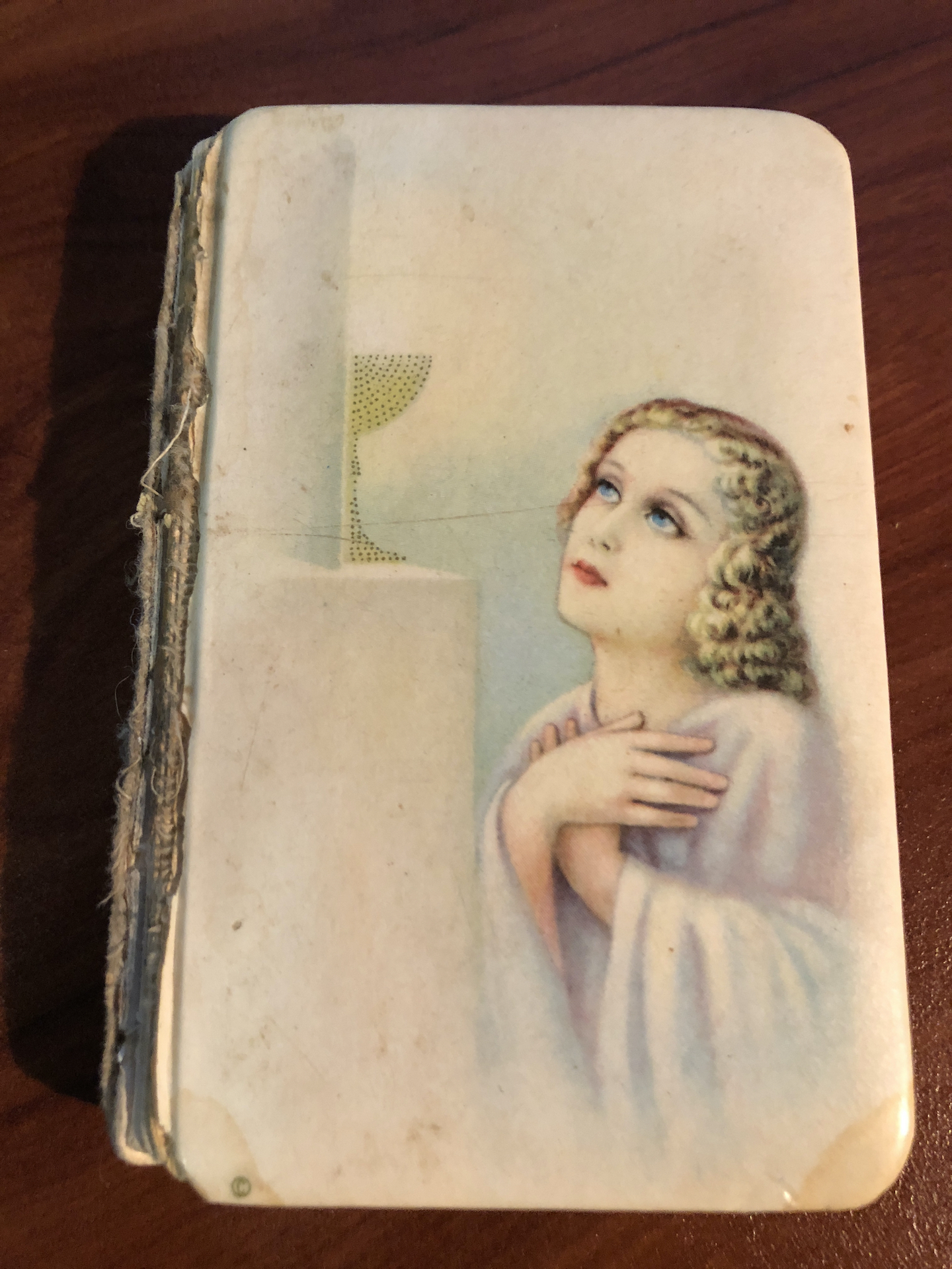 A tattered children's prayerbook with a young woman looking up at a statue adoringly.