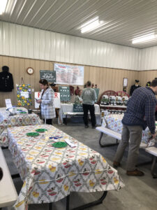 Large tables with paper plates, spoons, and seed packets in foreground. An information table with people gathered around it in background.