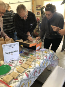 Two white men sort through a cardboard box of seed packets.