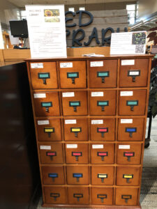 A wooden cabinet with small drawers. They are closed, but they are labeled and contain seeds.